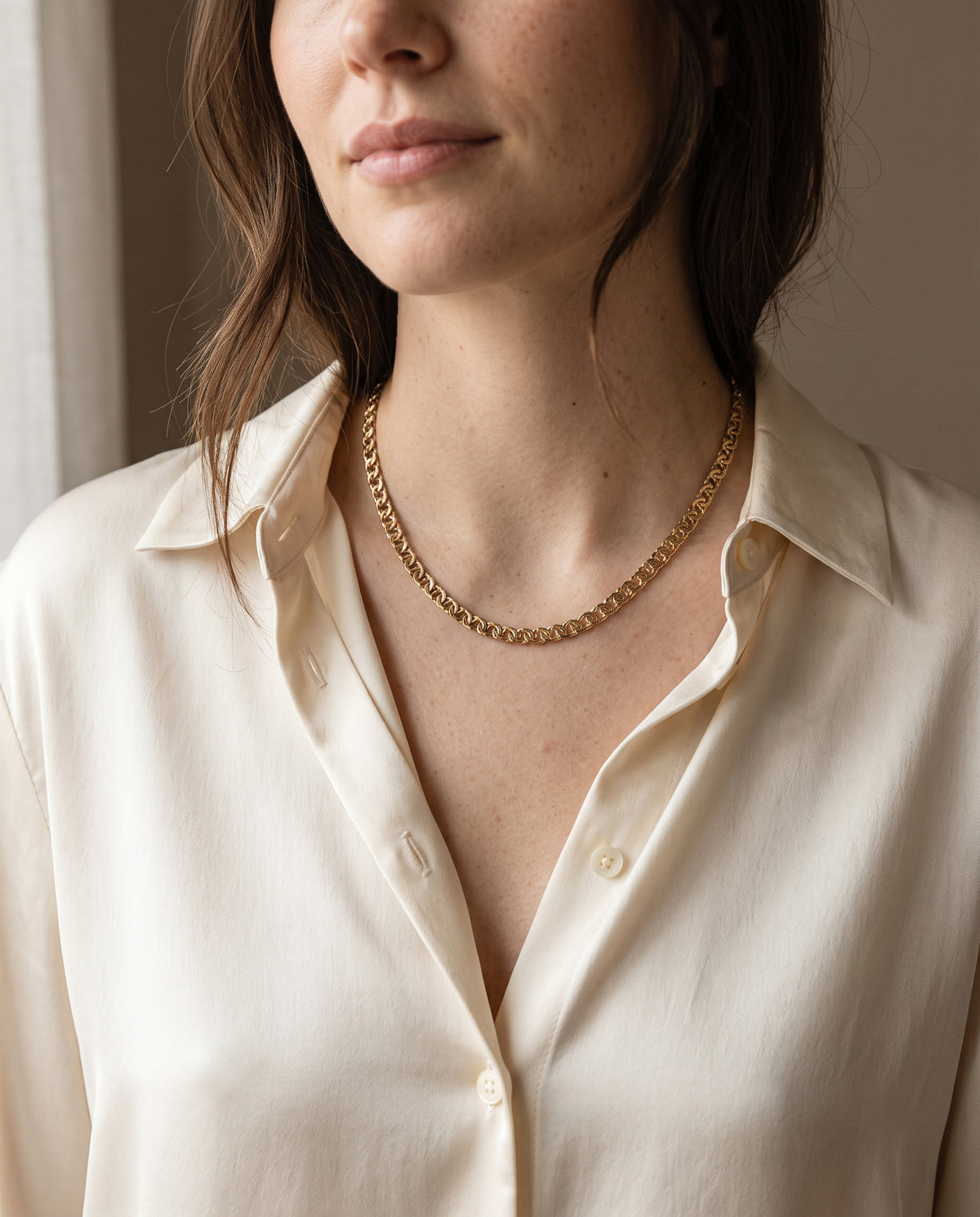 Woman wearing a gold-tone interlocking link chain necklace with a cream silk shirt, Artificial Arcana necklaces coming soon