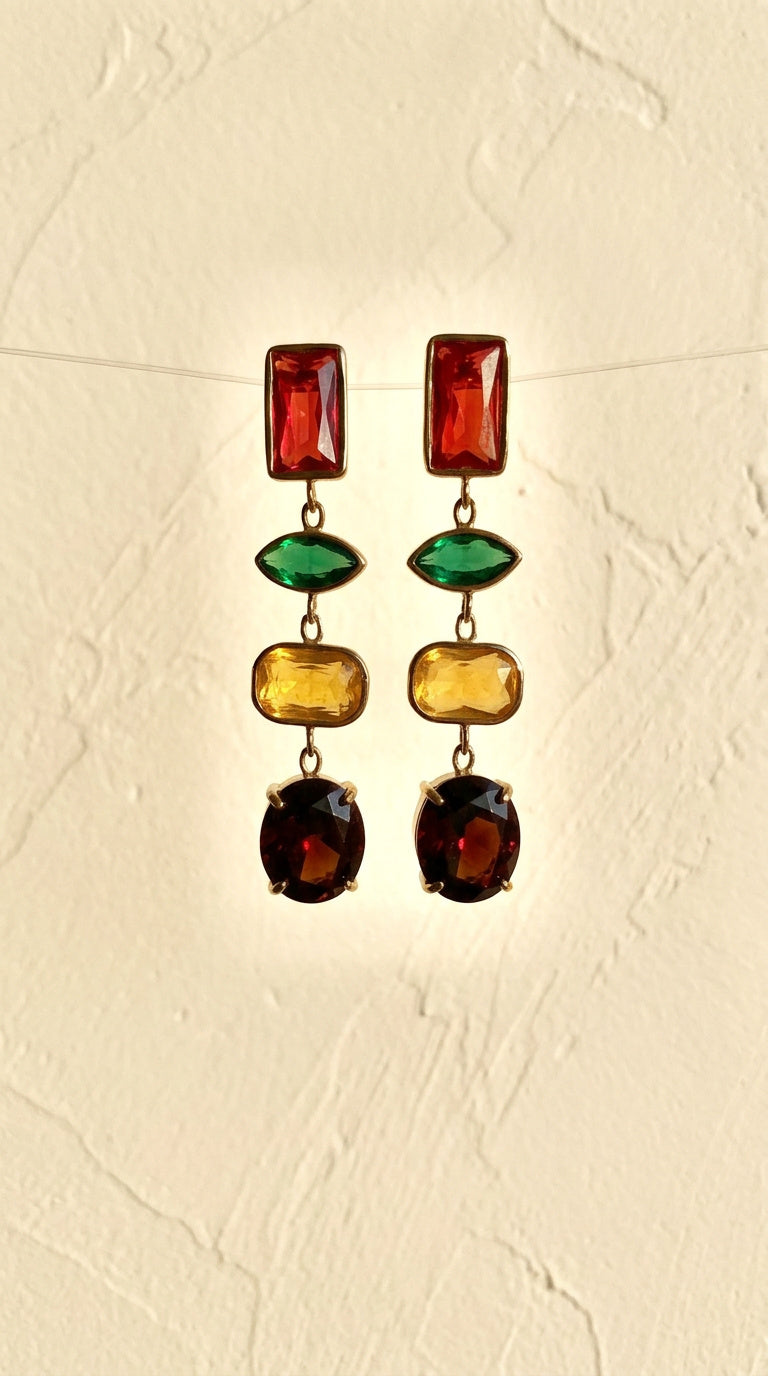 A pair of gold-tone dangle earrings with multiple colored gemstone drops, displayed against a textured beige background.