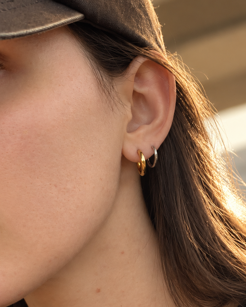 A close-up side profile of a woman wearing a small gold hoop earring, a dark brown cap, and a black t-shirt.