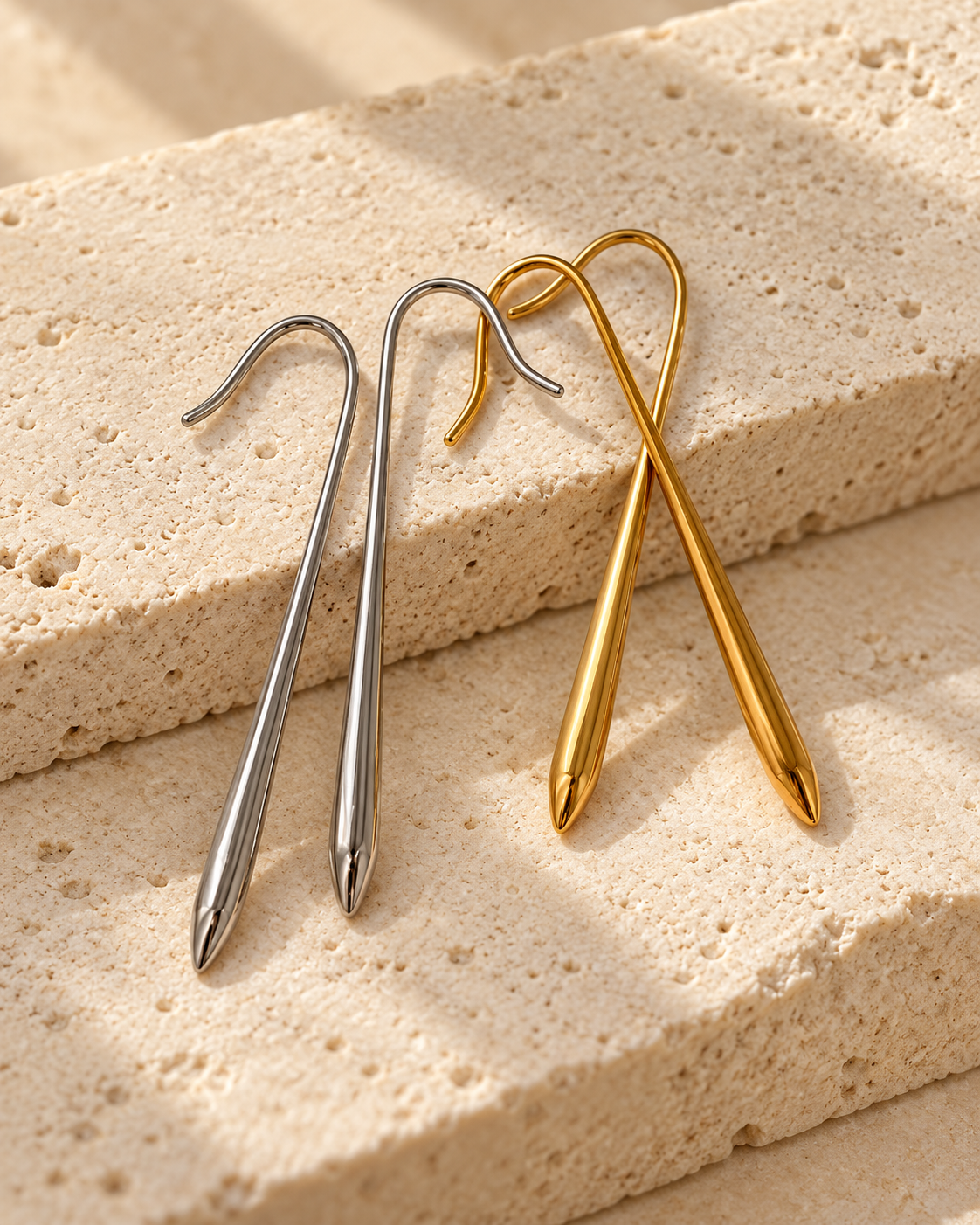 Two minimalist spiral drop earrings, one in polished silver and one in polished gold, displayed on textured beige stone blocks.